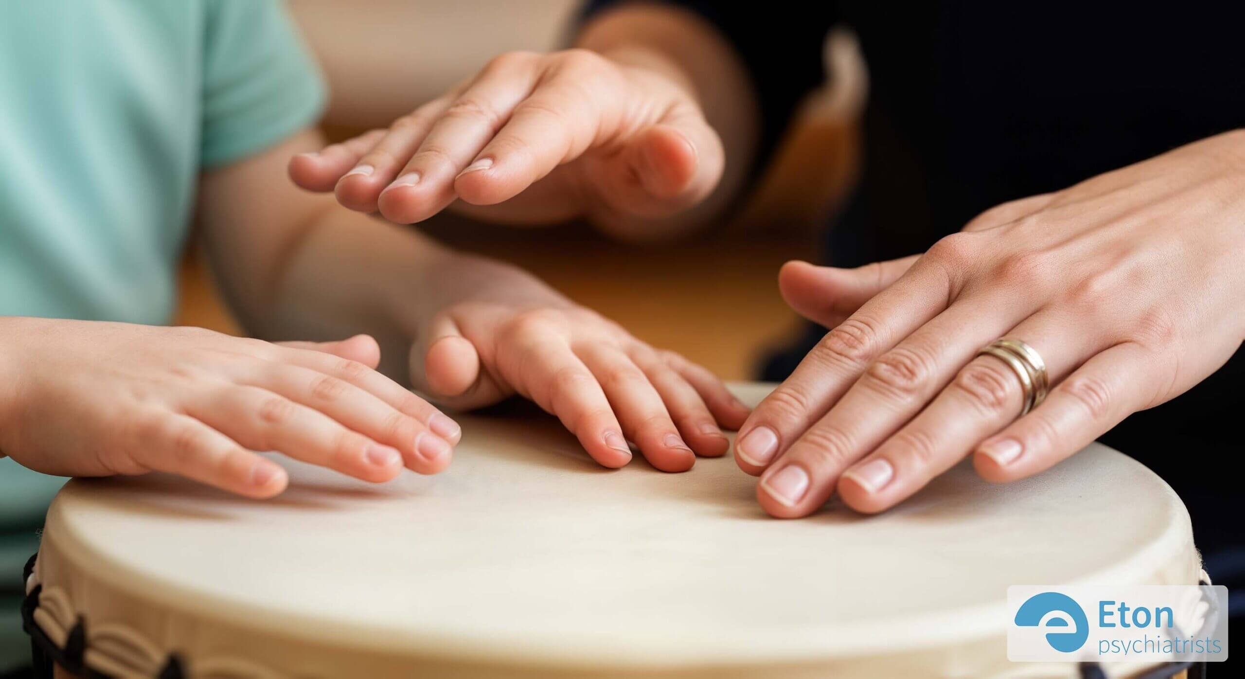 A close-up of a child's hands and a therapist's hands on a single hand drum, showing connection through music therapy.