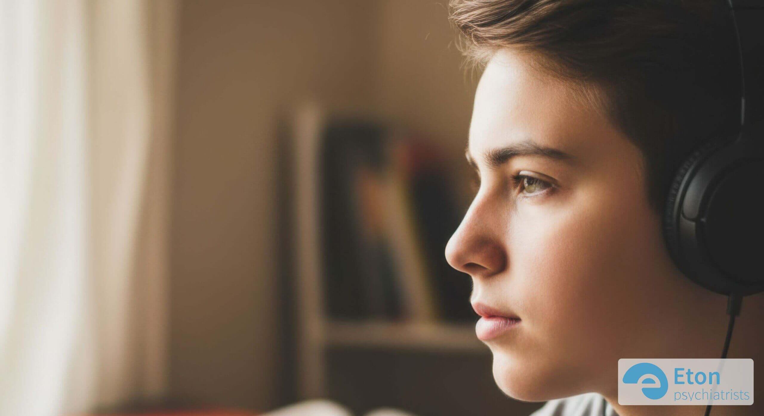 A thoughtful teenager with headphones looking out a window, representing the introspective and complex inner world of neurodivergent adolescence.