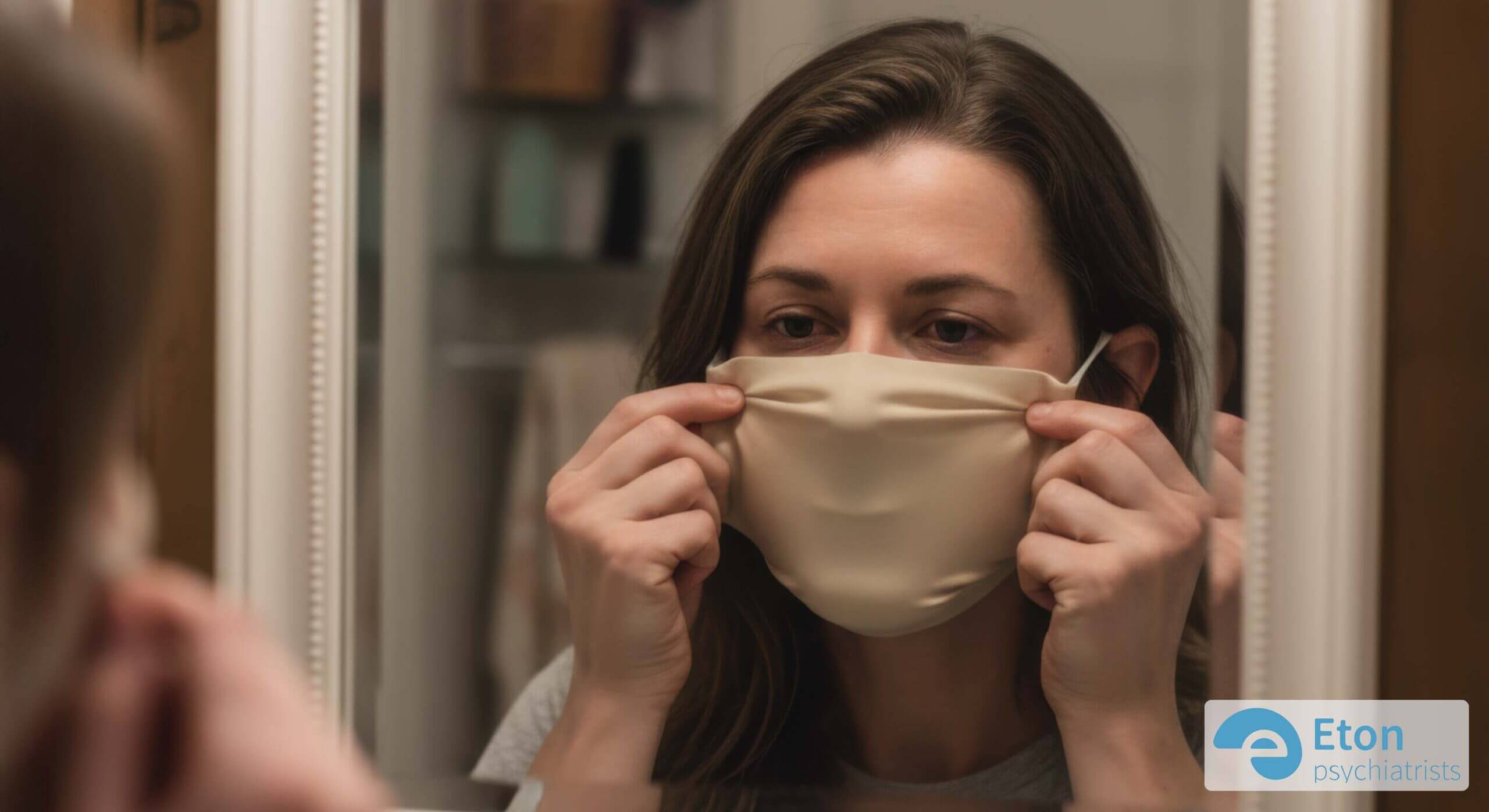 A woman adjusting a neutral mask over her reflection in a mirror, symbolizing the effort of ADHD masking.