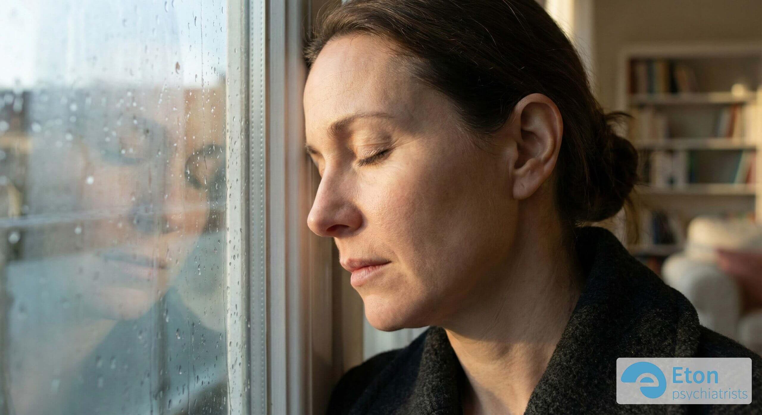 A woman leaning her head against a rainy window, looking tired and reflective.
