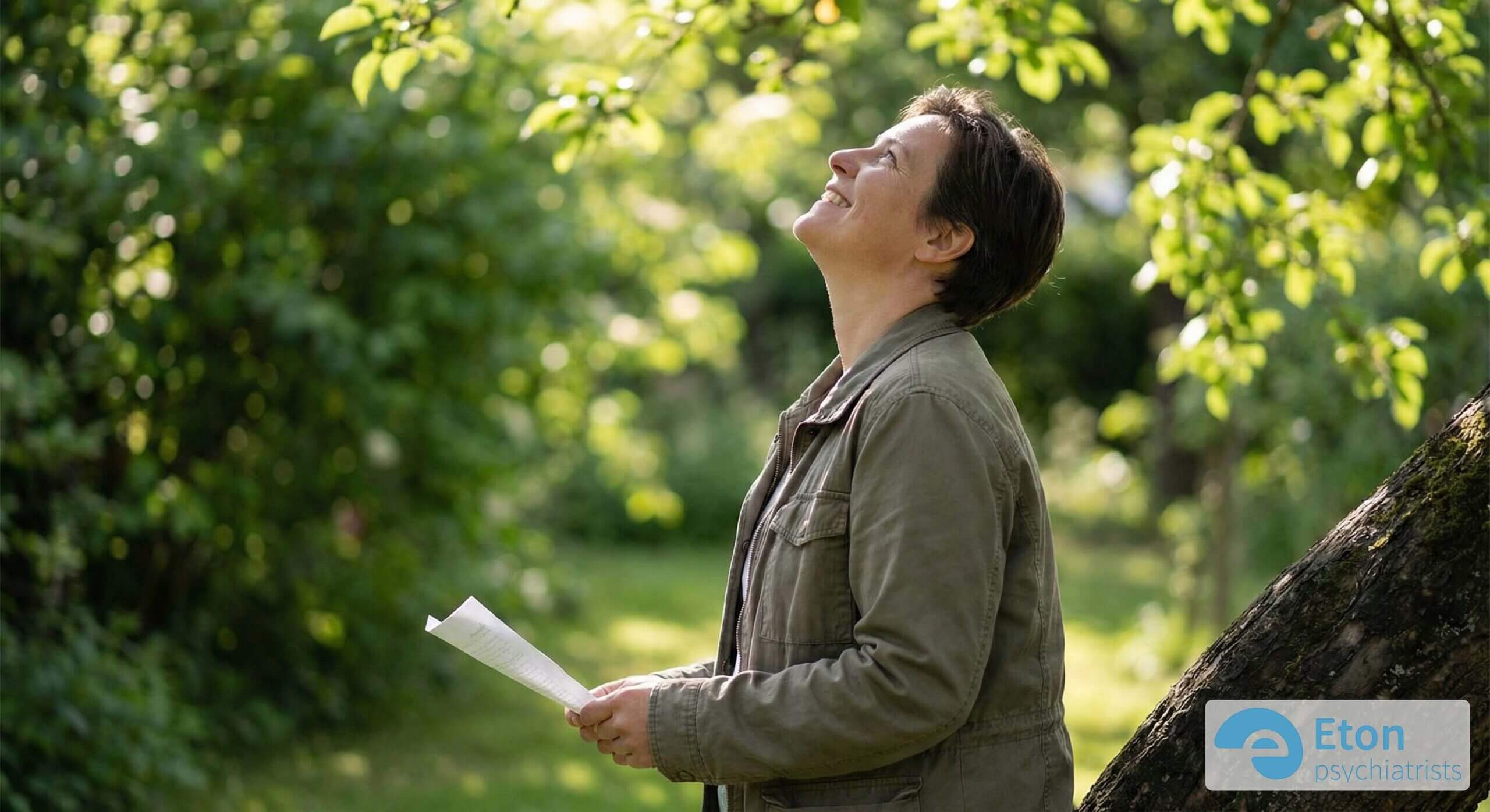 A woman standing among green trees looking upwards with a smile, symbolizing the relief and clarity of understanding oneself.