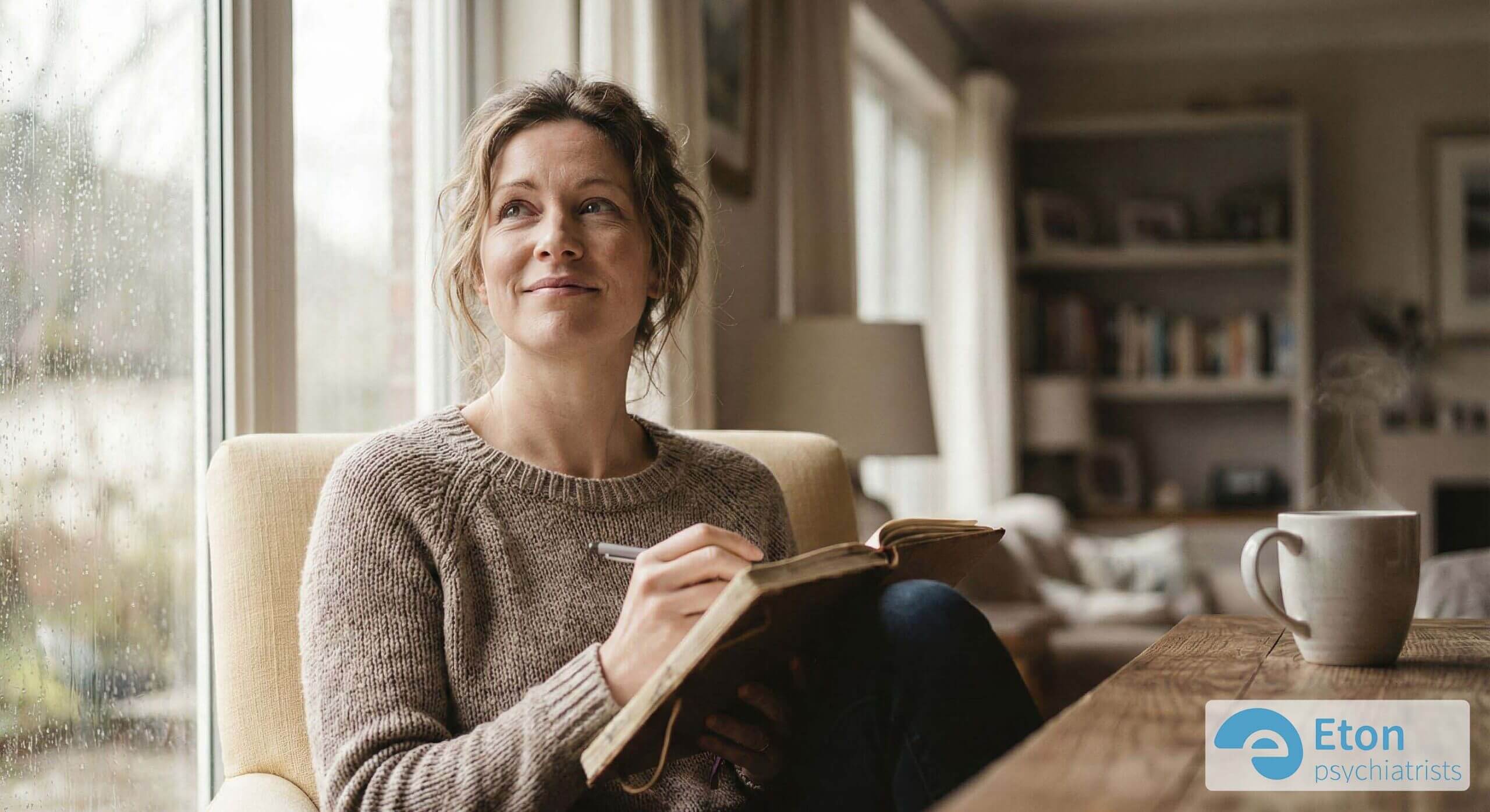 A woman looking out a window holding a journal, reflecting on her thoughts.